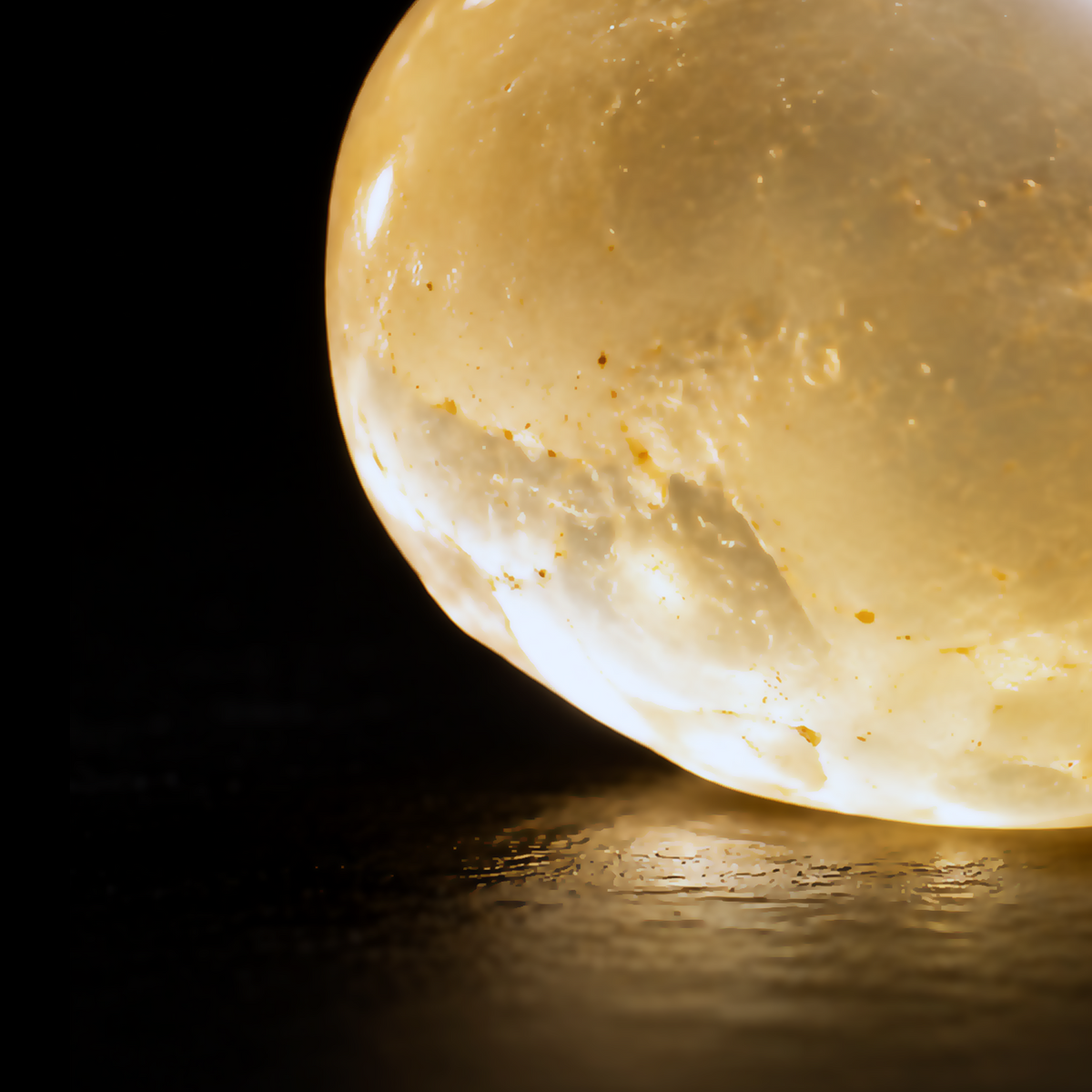 Extreme macro detail of a glowing translucent golden Chios mastic resin tear against a black background.