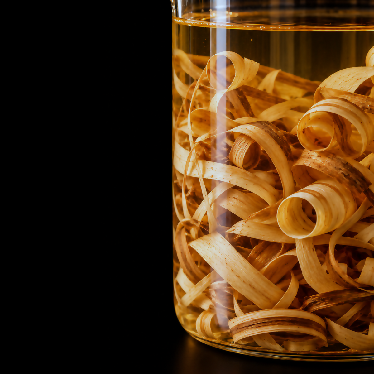 Ultra-macro view of curled Palo Santo wood shavings immersed in pale amber liquid inside a clear glass vessel against a black studio background