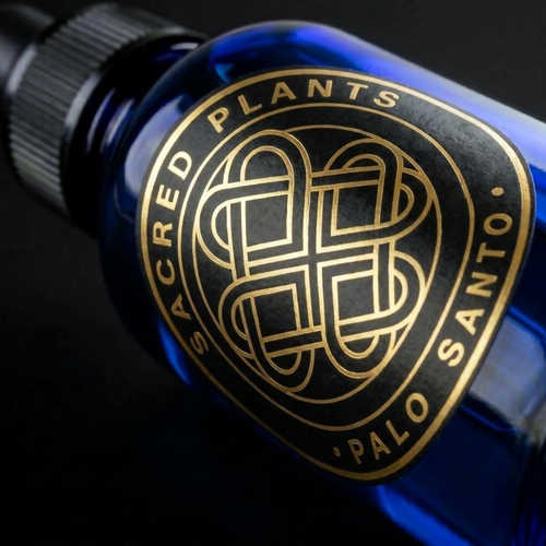 Macro photograph of a cobalt-blue glass Palo Santo oil bottle with a black and gold Sacred Plants Australia circular label