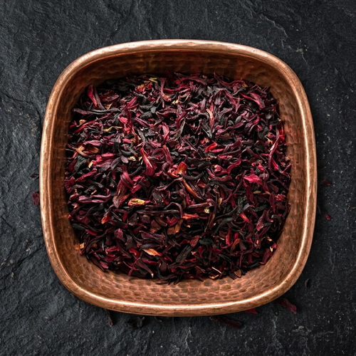 Dried Hibiscus × rosa-sinensis flower petals in a hammered copper bowl on a dark stone surface