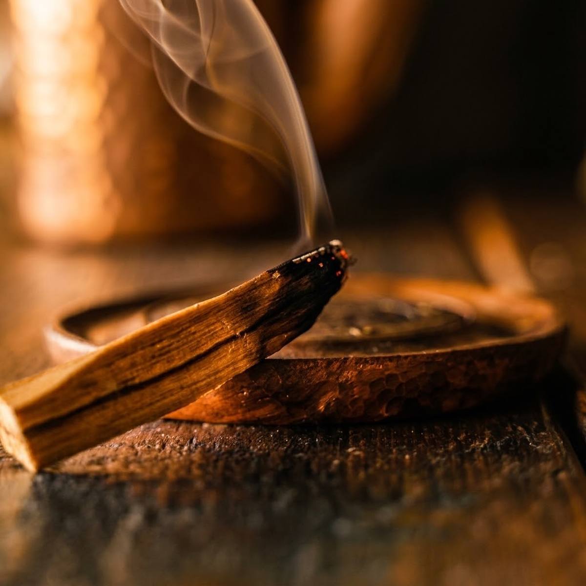 Peruvian Palo Santo stick smouldering over a copper bowl