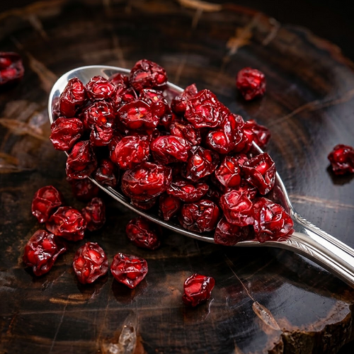 Whole dried Schisandra chinensis berries on a silver spoon against dark timber.