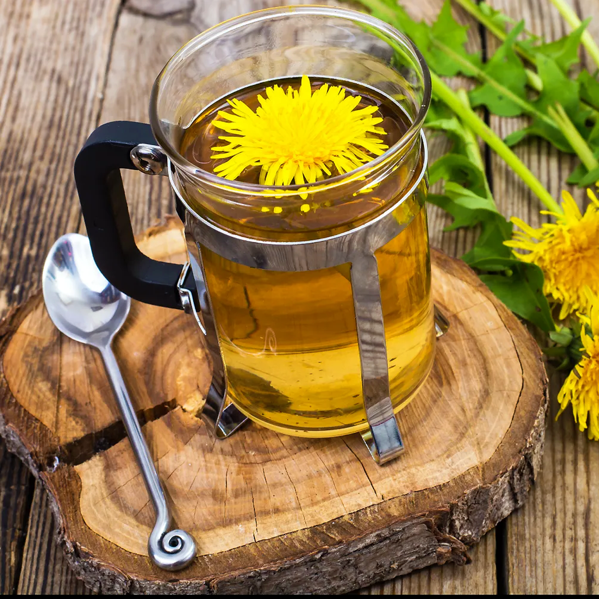 Golden dandelion tea in a glass cup with a yellow dandelion flower, presented on a wooden slab