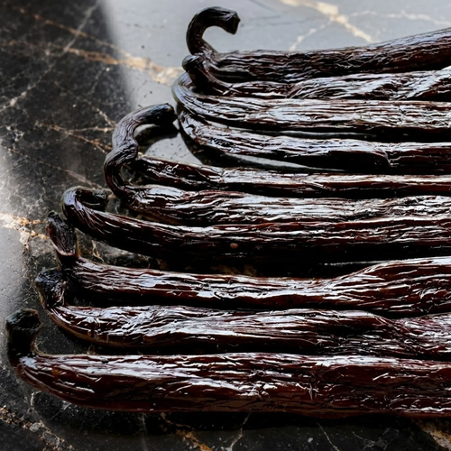 Sacred Plants Australia Madagascar Bourbon Vanilla Beans (Vanilla planifolia), close-up of multiple dark glossy cured whole vanilla beans arranged on black marble