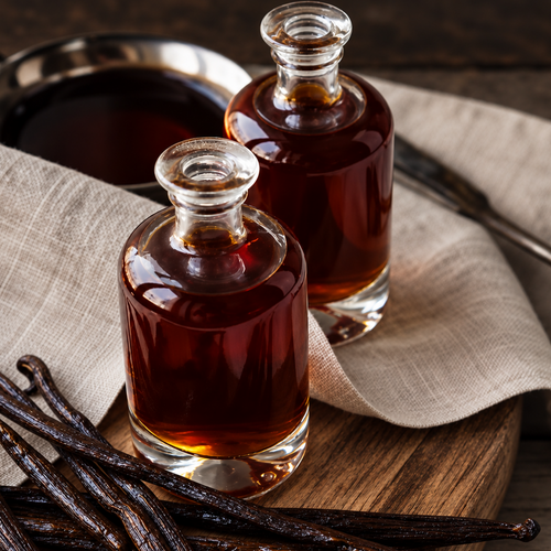 Sacred Plants Australia Madagascar Bourbon Vanilla Extract, Vanilla planifolia, two glass bottles of amber vanilla extract with vanilla beans on wooden board.