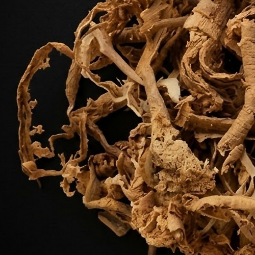 Extreme close-up of curled tan-brown Sananga root bark ribbons and porous woody fragments on a black background.