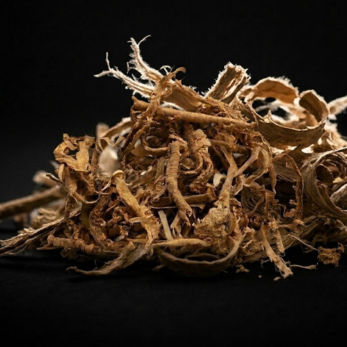 Side-view macro photograph of a loose mound of dried tan-brown Sananga root bark, showing curled strips, woody fragments and pale fibres against a black background.