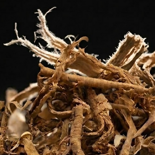 Close-up of dried Sananga root bark showing pale split fibres, curled strips and woody fragments against a black background.