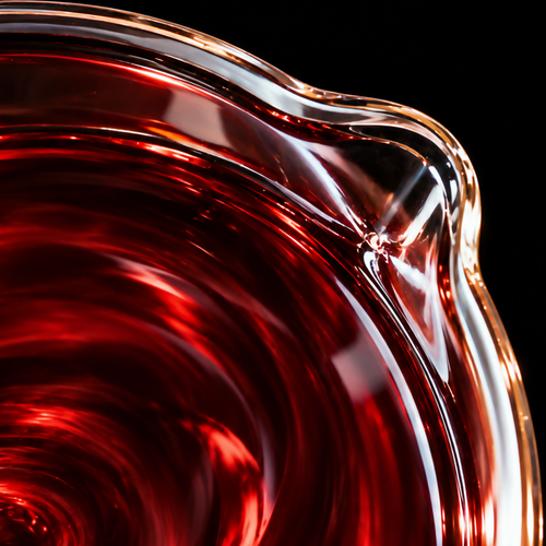 Extreme macro photograph of crimson Dragon's Blood infused oil swirling in a clear glass beaker, with its pouring spout in the foreground