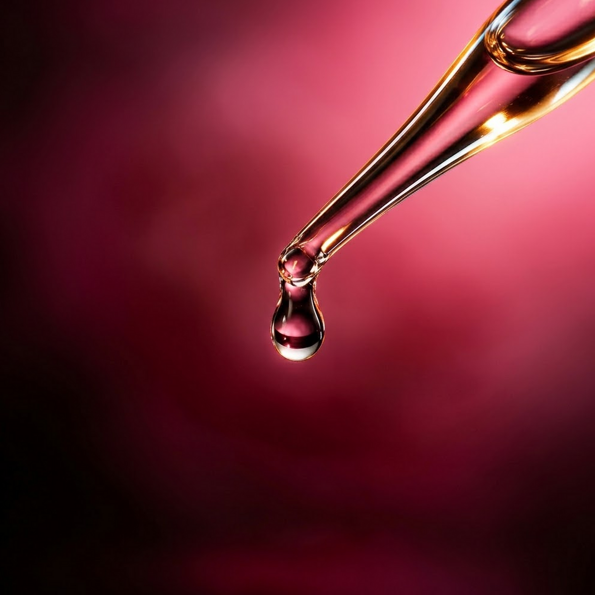 Damask Rose Hydrosol, clear droplet suspended from a glass pipette entering from the upper right against a rose-pink background