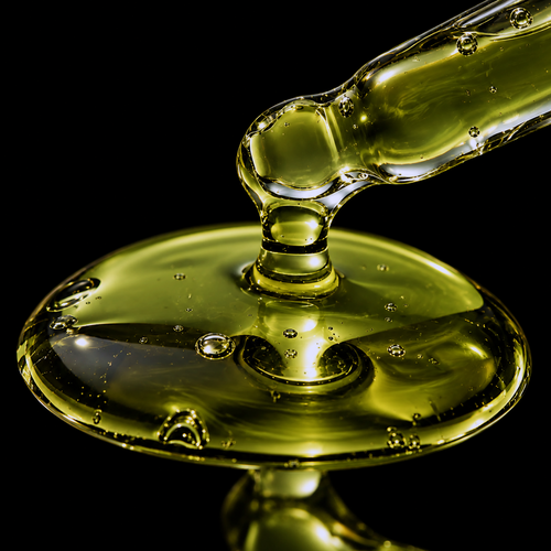 Ultra-macro of olive-green Vanuatu tamanu oil flowing from a glass pipette into a glossy pool against a black background